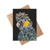 Greeting card with a colorful parrot illustration on a black background, placed on a brown envelope.