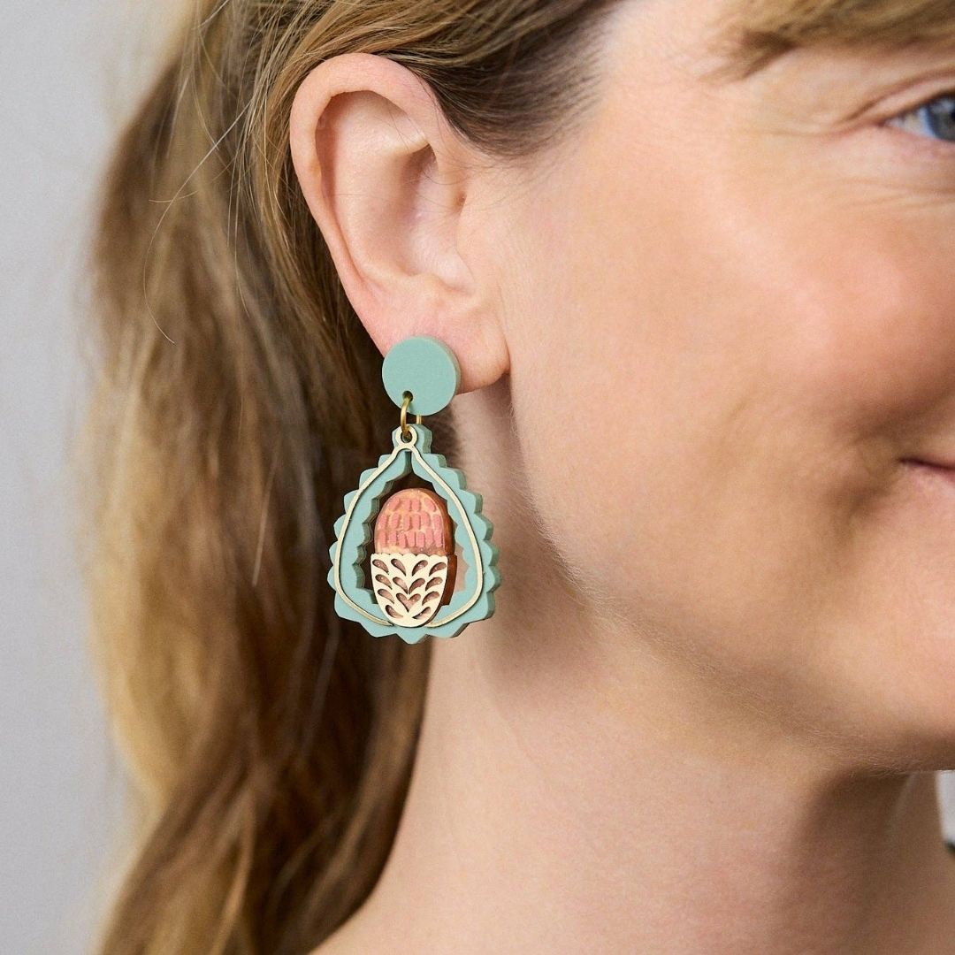 Pair of earrings with pink and gold banksia design on a light green background