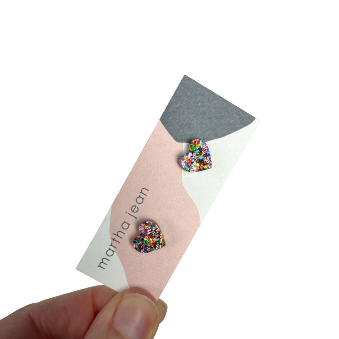 Colorful rainbow heart-shaped earrings on a 'martha jean' card held by a hand.