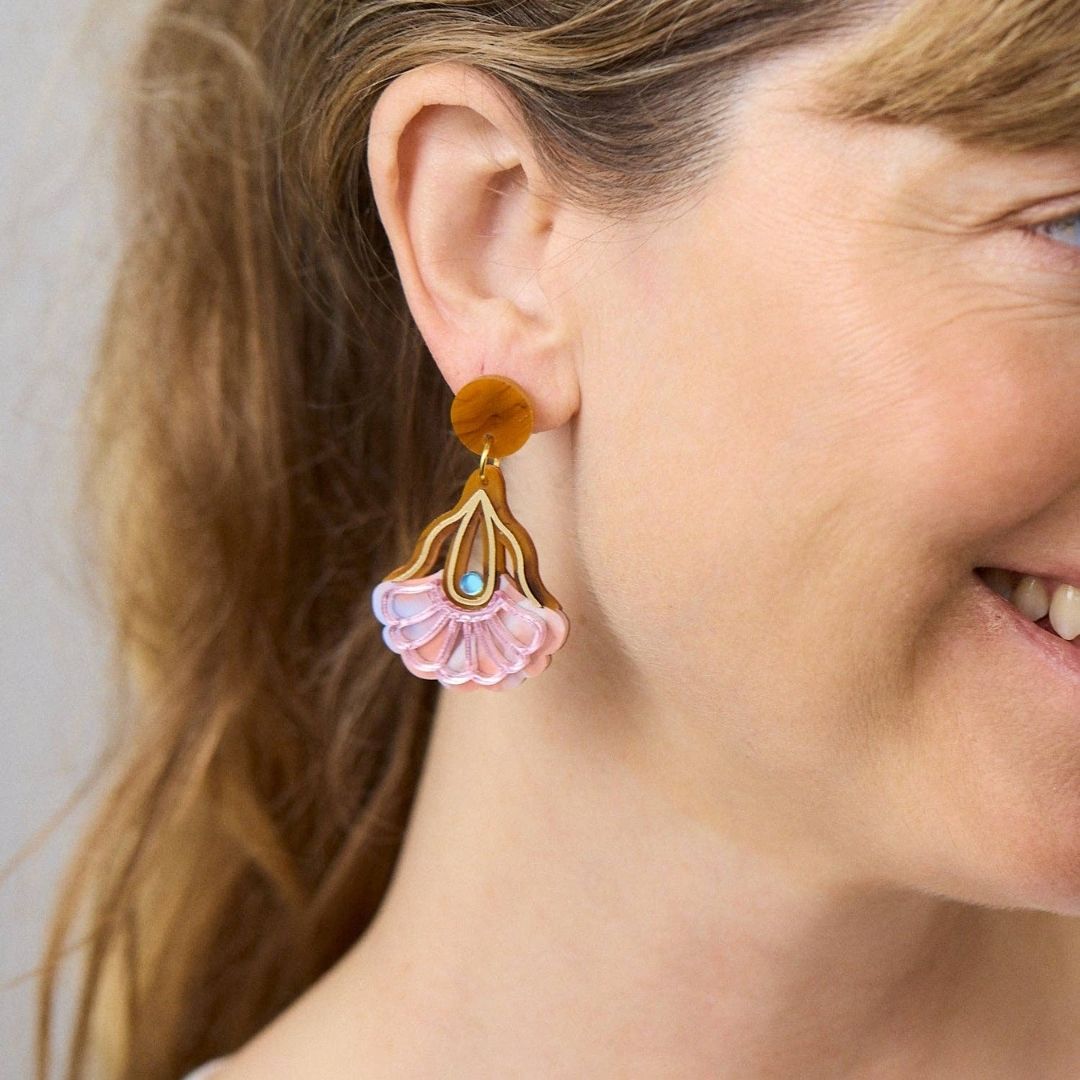 Pair of earrings with pink and gold floral design on a white background