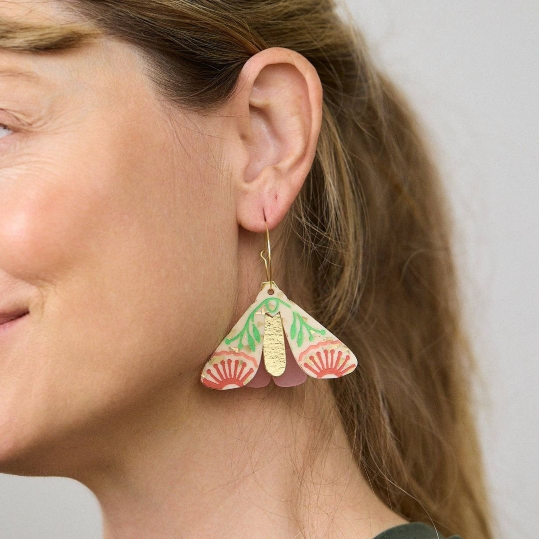 Pair of moth-shaped earrings with pink, green, and gold design on a white background