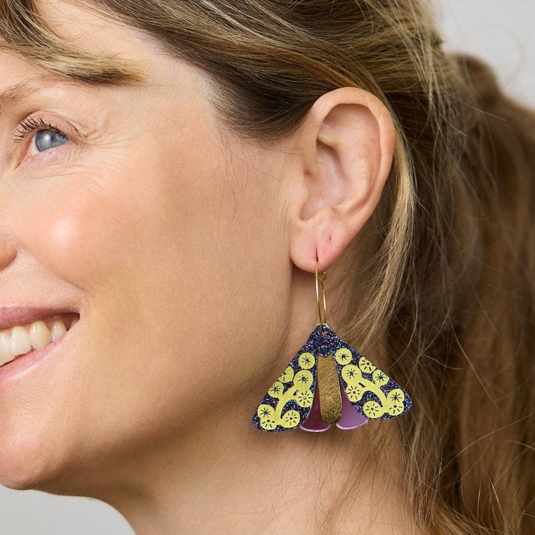 Pair of midnight sparkle moth-shaped earrings with yellow wattle patterns on it, on a white background